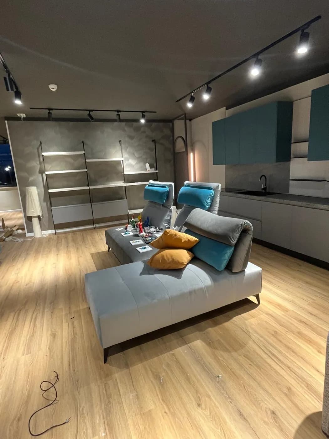 Zona living con libreria a parete, divano componibile e cucina sullo sfondo
